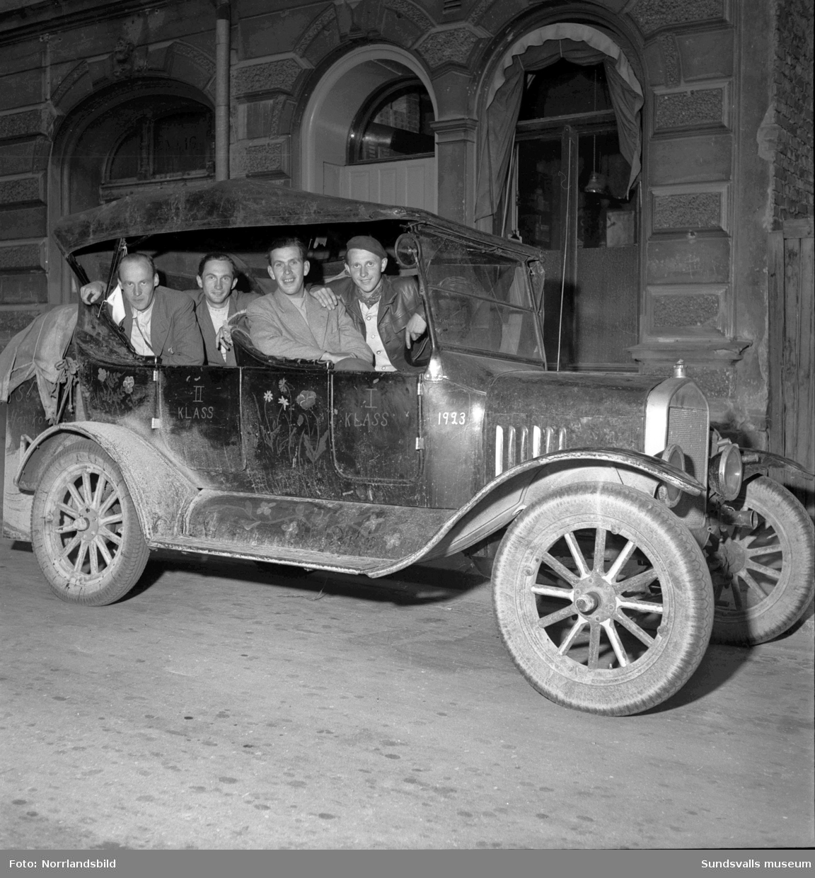 Fyra skånegrabbar på turne med en motivlackad Ford från 1923, registreringsnummer L12872. Parkerad vid Trädgårdsgatan 16 väcker de stor uppmärksamhet.
