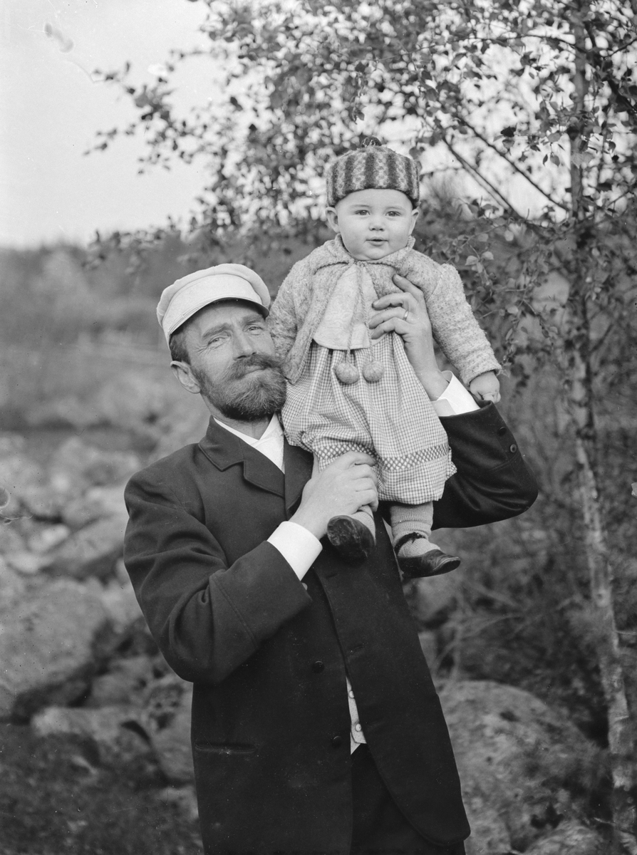 Komminister Carl Manneberg med yngste sonen Allan på axel. Familjen var bosatt i kaplanbostället Skuru under åren 1891-1915. Allan blev sedermera kriminalkonstapel i Stockholm. Året är 1891.