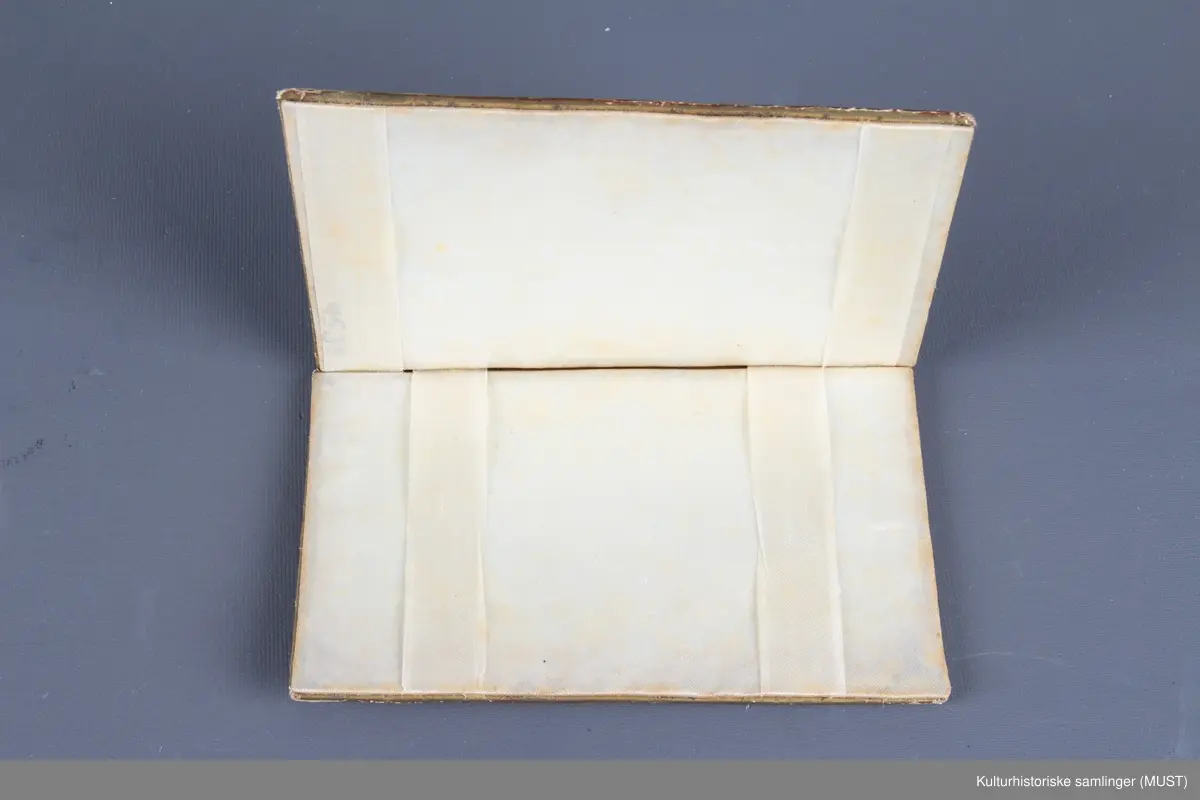 Visittkortmappe av papp. Permene består av hvit, perforert pappkartong og hvit silke. På permene korsstings- og perlebroderier, langs kanten en "gullist".