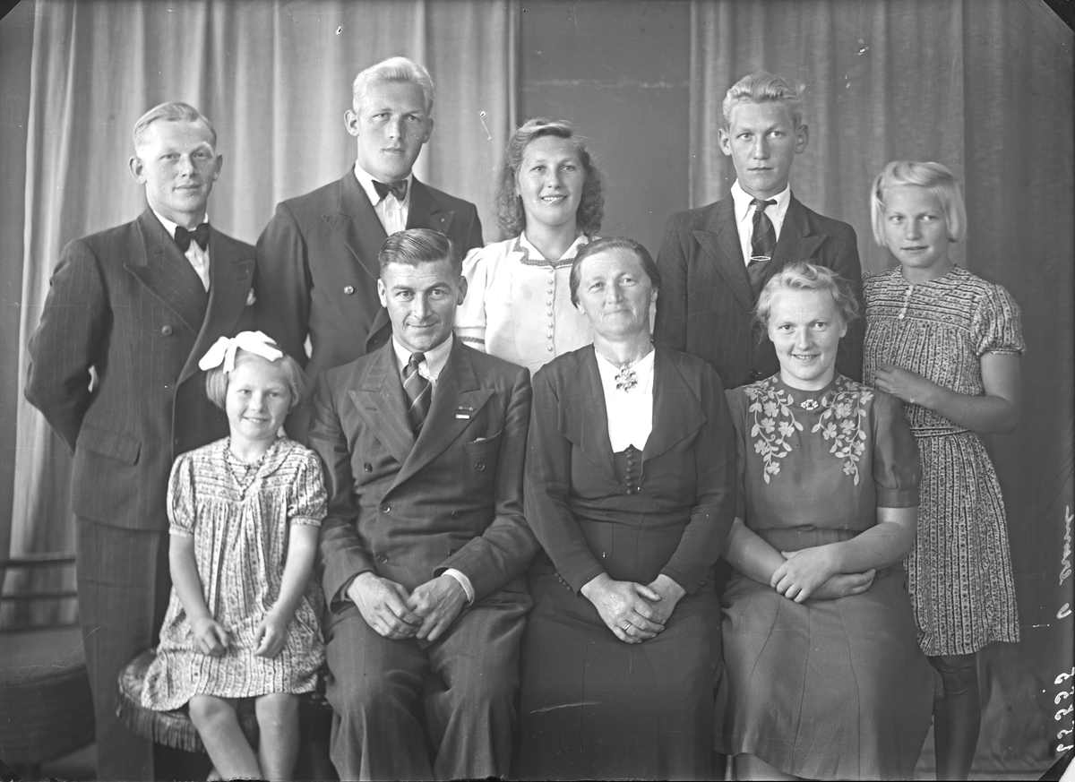 Gruppebilde. Familiegruppe på ni. Mann, kvinne, tre unge menn, to unge kvinner og to piker. Bestilt av Johan Rossehaug. Sveio.