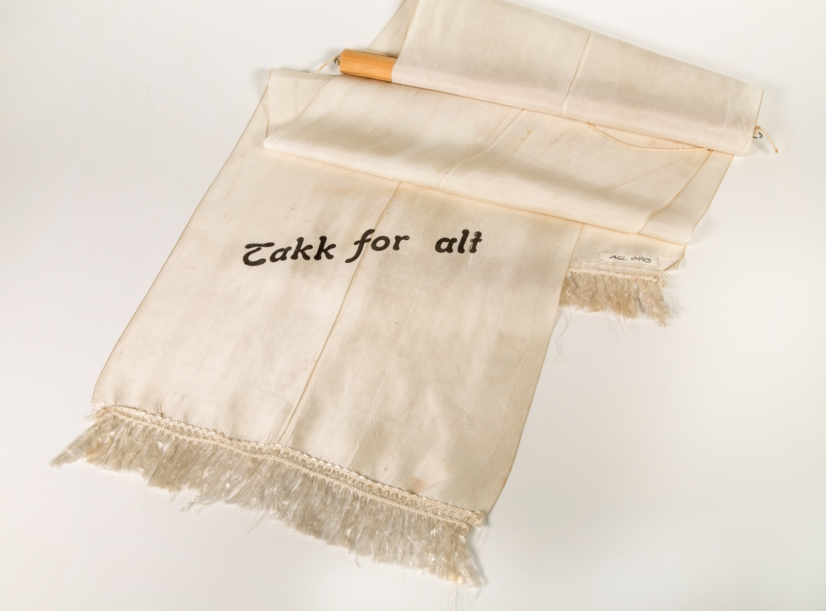 Stort sørgebånd til begravelse. Festet til rundstokk for oppheng på vegg. Til Garborgs begravelse.