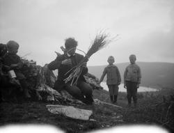 Tre smågutter står å se på en ung menn som sitter ved på ei 