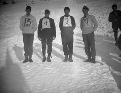 Fire deltagere med nummer på brystet står i bakken uten ski.