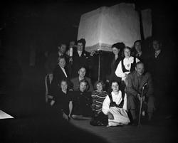 Gruppe mennesker samlet rundt peisen med Alfred Maurstad på 