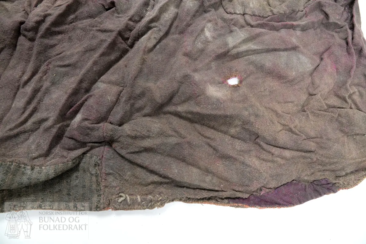 Del av ein stakk, full høgde utan linning. To høgder av brun og lilla verken, lerretsbinding med ull i innslag og renning, sauma saman for hand. Stoppa med eit stort stykke midt på høgda og to gonger i nedkant, truleg med sama stoff som stakken, bortsett frå eine bota i nedkant som er eit stripete stoff i raud, svart og brunt. Framstår som utslitt i fargen med fleire hol etter mus, har vore nytta som stappefille.