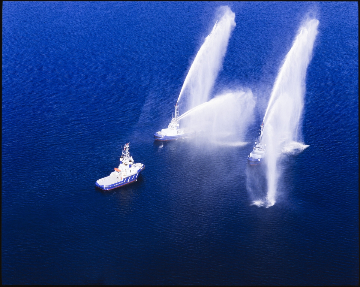 To av tre taubåter spruter vann i ulike retninger på sjøen.