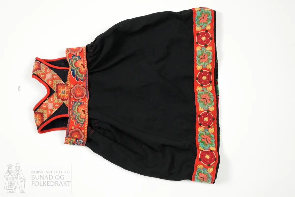 Liv sauma av fast tjukk mørk blå vadmål, påsett kelimvovne band som kryssar midt bak på ryggen. Kanta med raude kypertvovne ullband. Heile livet maskinsydd. 
Stakk sauma av krosskypertvove svart tynt stoff av syntetisk materiale. Stakken har løpegang med snøring oppe i livet. I nedkant og øvrekant er påsydd raude ullband med plattsaumsroser av anelinfarga ullgarn. Bandet oppe i livet er kun fastsydd i øvrekant og ligg laust utanpå stakken. 
Forkle fastsydd til det broderte ullbandet, av trykt kypertvove ullmusselin. 
Heile stakken maskinsydd.