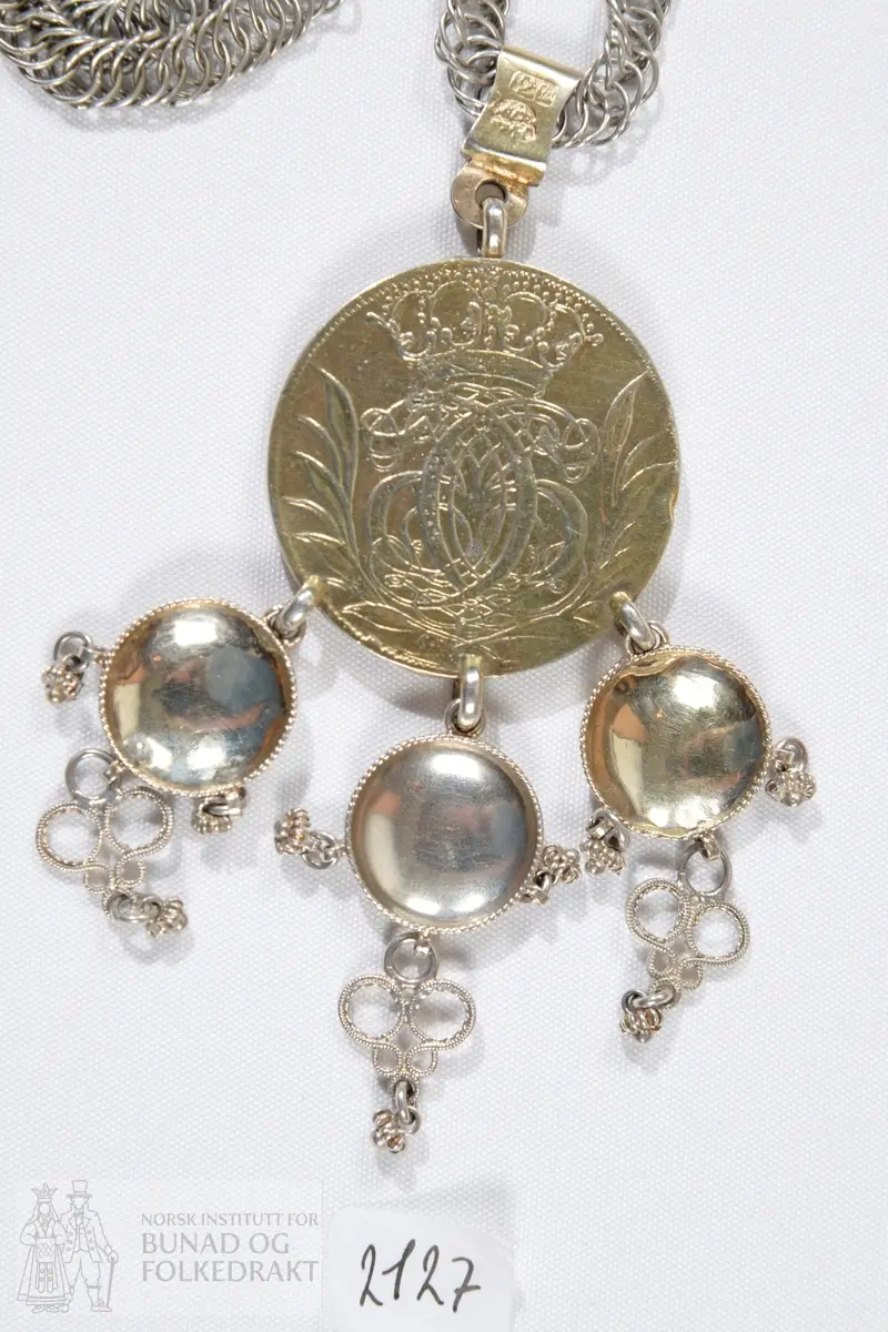 Brudedaler med breikjede. Breikjede er satt sammen av en rekke ringer av sølvtråd festet inn i hverandre. Forgylt mynt med tre ringer påloddet, fra disse henger tre skålformede løv med trådkant, filigranspynt og kruser. Myntens forside: Kronet speilmonogram omgitt av krans. Myntens bakside: Kronet våpen med tre løver, årstallet 1693. Mynten henger i et sølvband på kjedet. På dette bandet er det stemplet: IMS på det ene siden, 12L og gardeinstempel MB 1740.
IMS står for sølvsmed Jacob Michelsen Steen, fra Bergen og med borgerbrev fra 1722. 12L står for 12 lodd, lødigheten i sølvet. De tre skålene er ikke stemplet. 
Mynten er dansk-norsk med Christian den 5.'s speilmonogram, merket 1693.