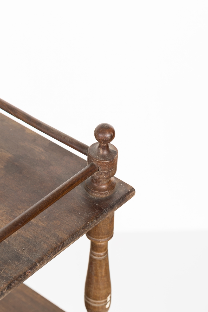 Hylle med 4 hyller. Dreide stolper mellom hyllene. Mangler ett bein. Sprosser øverst. Lakkert i mørk brunt.