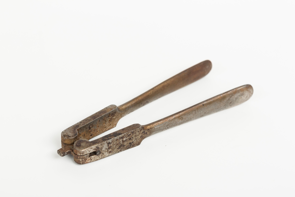 Nøteknekker i stål uten dekor. Utslåtte knaster på "gripeflatene". Hengsel med avstandstykker for to knekkeavstander.