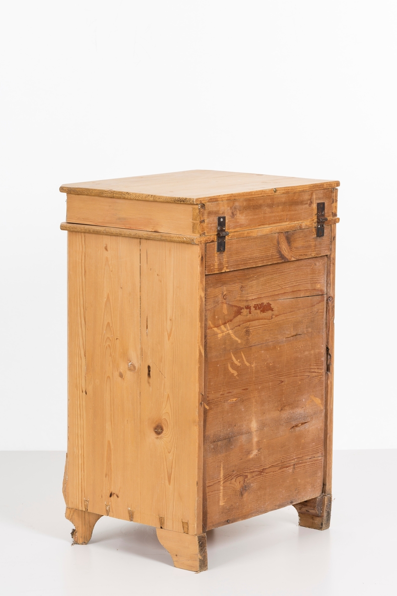 Toalettbord i ubehandlet tre. Det er rom for vaskebolle og skap under. Messingknott på døra til åpning og lukking, spor på innersiden av skapet kan tyde på at det tidligere også har vært en lås.