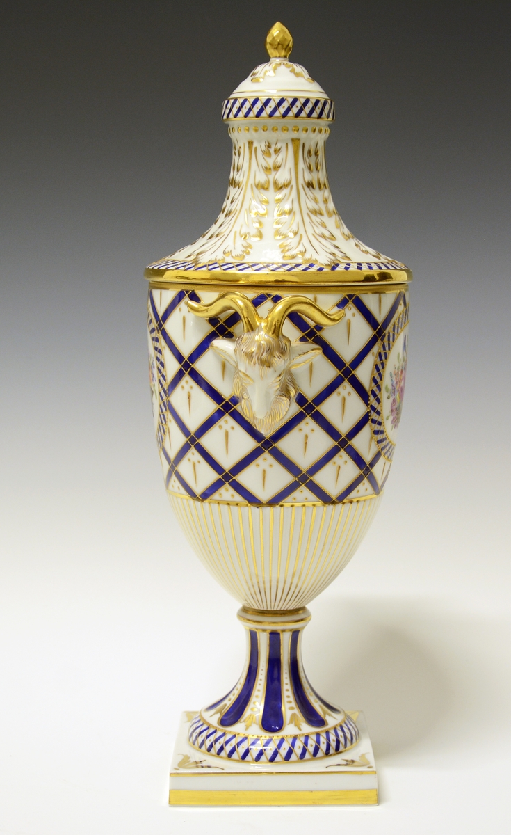 Potpourrikrukke av porselen med lokk. Hanker formet som bukkehoder. Håndmalt geometrisk dekor i blått og gull. I et ovalt felt på hver side håndmalt blomsterdekor. Sannsynligvis kopi av Sèvres, produsert ved en av de andre franske porselensfabrikkene.