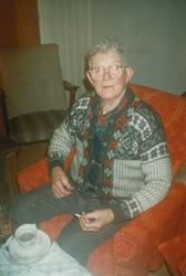 Eldre mann med lusekofte sitter i godstolen med en sigaretts