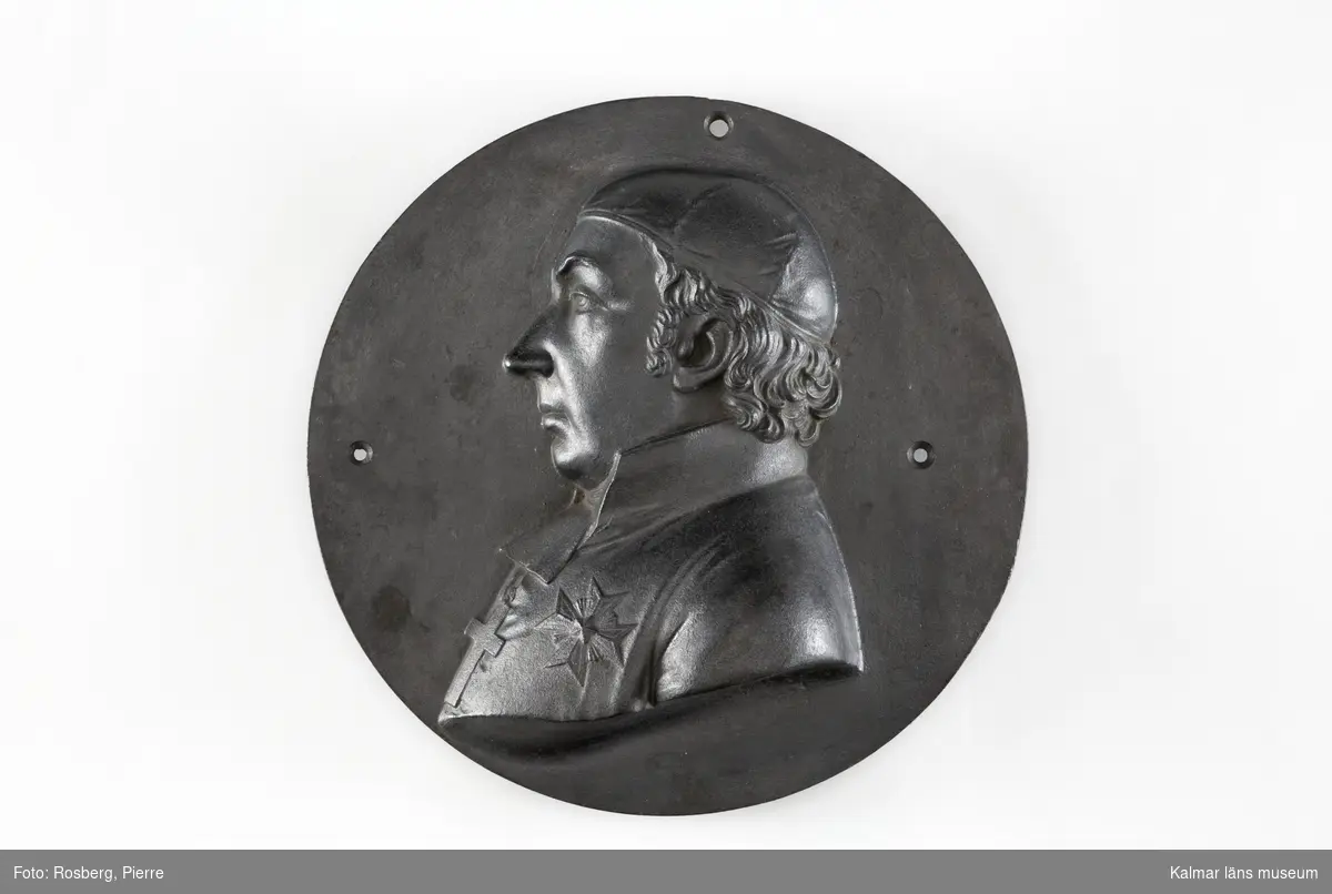 KLM 16524. Medaljong, porträttmedaljong, av gjutjärn. Rund. Relief, föreställande Ludvig Mörner, Växjö (1764 -1823). Bröstbild, vänd t.v. På huvudet kalott. Ingen signatur eller stämpel. Tre genomgående hål för uppfästning.