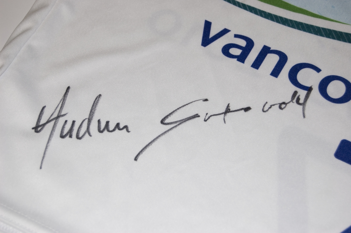 Flerfarget startnummer med nr. 7. På nummeret er det motiv av de olympiske ringene og to skicrosskjørere. Nummeret er signert.