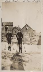 To gutter på ski. Bygninger i bakgrunnen.