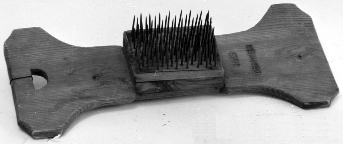 Linhekle av tre med et halmåneformet hull i den ene enden. Brettet smalner inn mot midten der det er en trekloss med stålnagler.