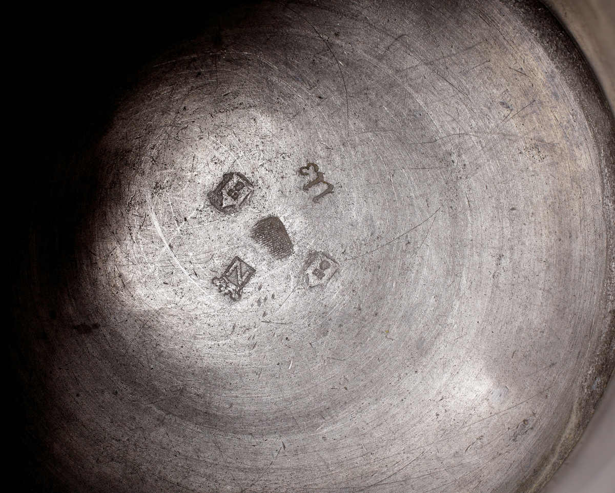 Stop i tenn, med lock.
Cylindrisk , något konande modell med enkel banddekor. Locket försett med infälld medalj (mynt?) över Karl XIV Johan (reg. 1818-1844). 
Stämplar på undersidan av stopet.