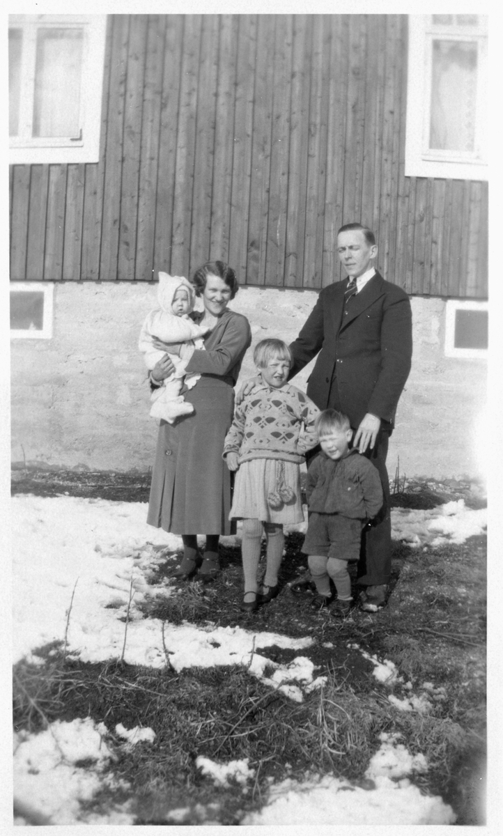 Familie fotografert foran en husvegg.