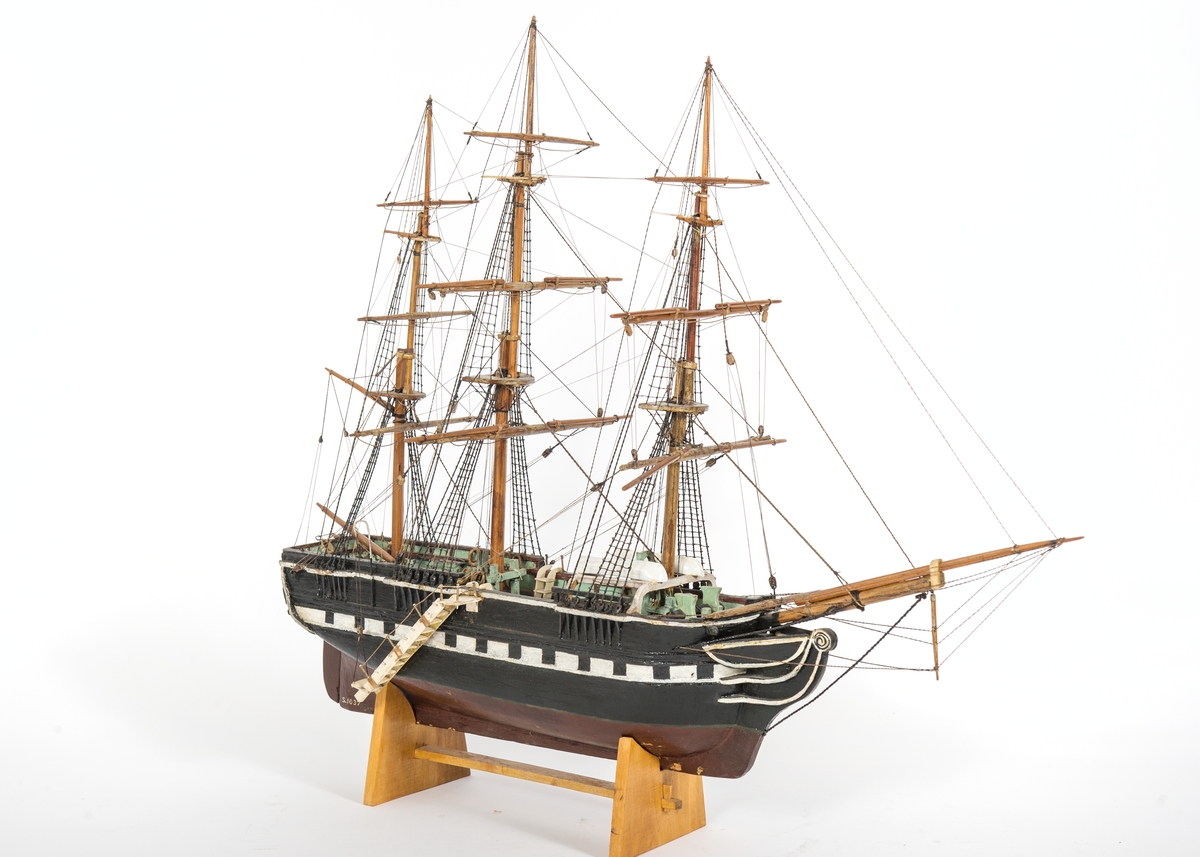 Fartygsmodell av fullriggat skepp utan segel med enkla märsrår. Akter om fockmasten galje med livbåt. Fallrepstrappa och lotslejdare av ben.