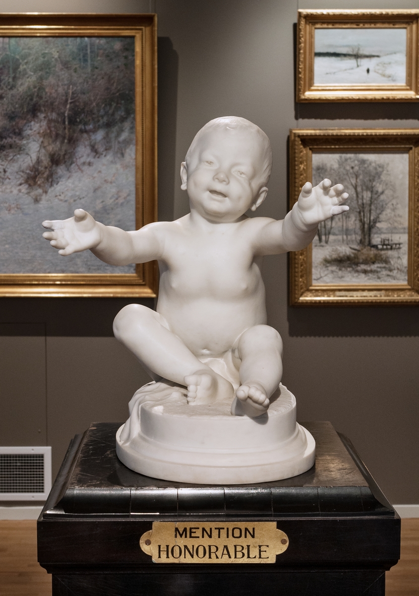 Skulptur i marmor föreställande litet barn med utsträckta händer. Skulpturen antogs till Salongen i Paris 1896, där Ida Matton bodde och verkade, och erhöll Mention Honorable, det högsta priset en kvinnlig konstnär kunde få på Salongen. 1-3:e pris kunde endast tillfalla manliga konstnärer. Podiet är original.