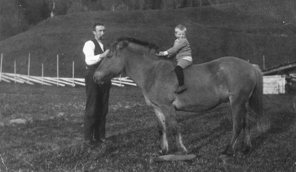 Georg Rosvold og søstersønn Roy Lindseth på besøk fra Amerika. Roy Lindseth sittende på hest og Georg Rosvold står på siden med pipa i munnen.