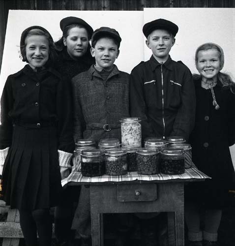 En grupp barn står stolta bakom en bord fullt med glasburkar med inlagda grönsaker. Unga Odlare 1948 - 1949.