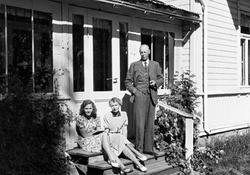 Familien Horst, to kvinner og en mann, sitter på trappen utenfor en villa.