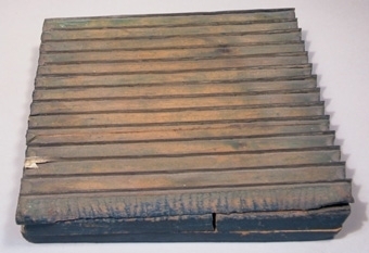 Tryckstock av trä med infällda metallskenor som vid tryckning bildar ränder. Undersidan är målad blå.