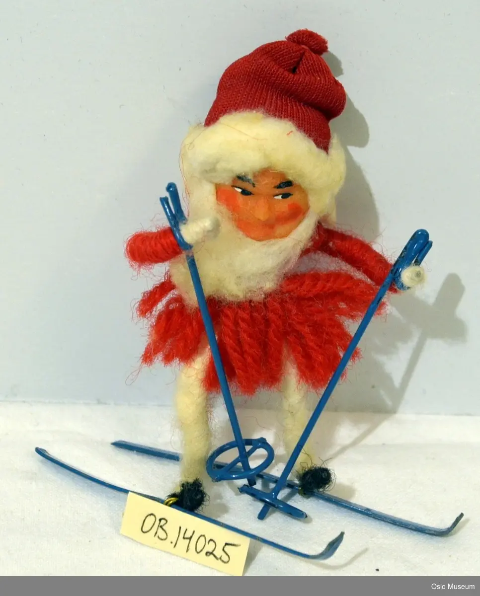Liten julenisse på ski til pynt, laget av garn og stål.