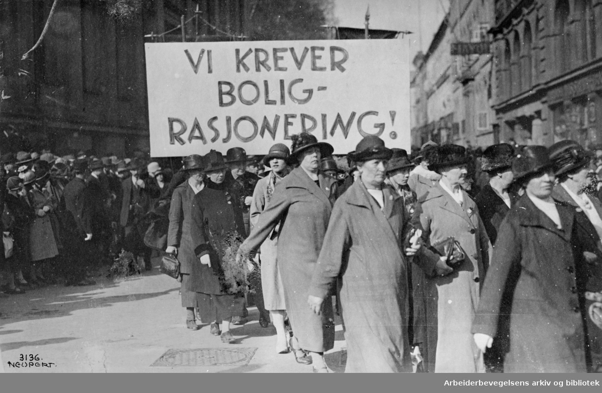 1. mai 1925, Arbeiderpartiets kvinneforeninger i Oslo. Demonstrasjonstoget svinger inn på Karl Johans gate fra Universitetsgata. Parole: Vi krever boligrasjonering!..