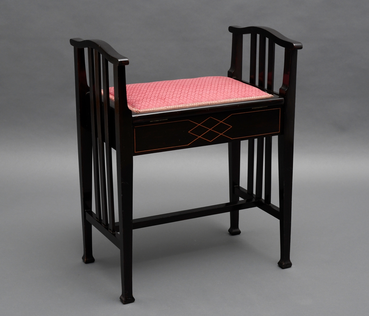 Pianokrakk, av tre, svart lakkert med intarsia. Et rom under setet, setet er hengslet og har tekstiltrekk.