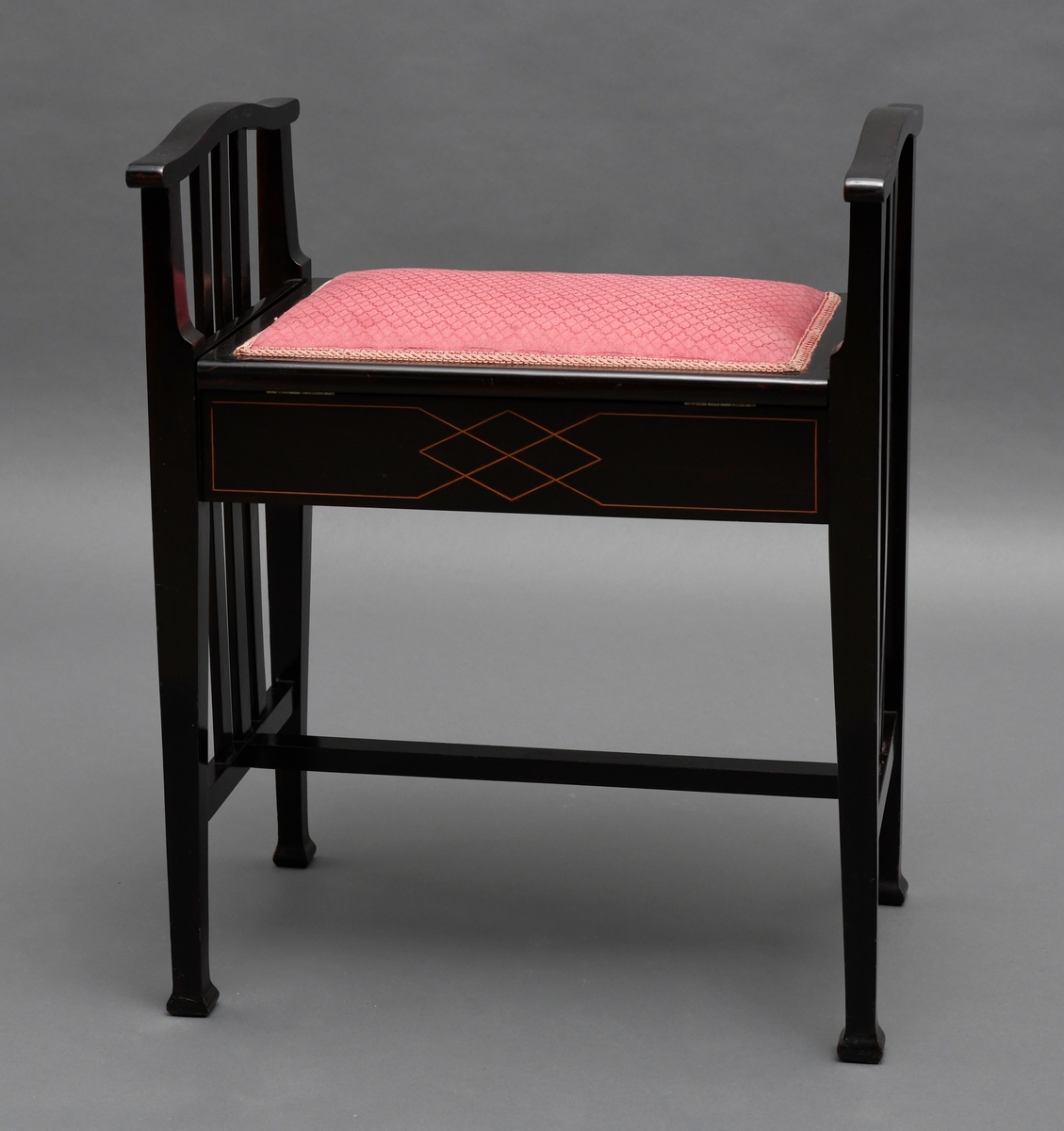 Pianokrakk, av tre, svart lakkert med intarsia. Et rom under setet, setet er hengslet og har tekstiltrekk.