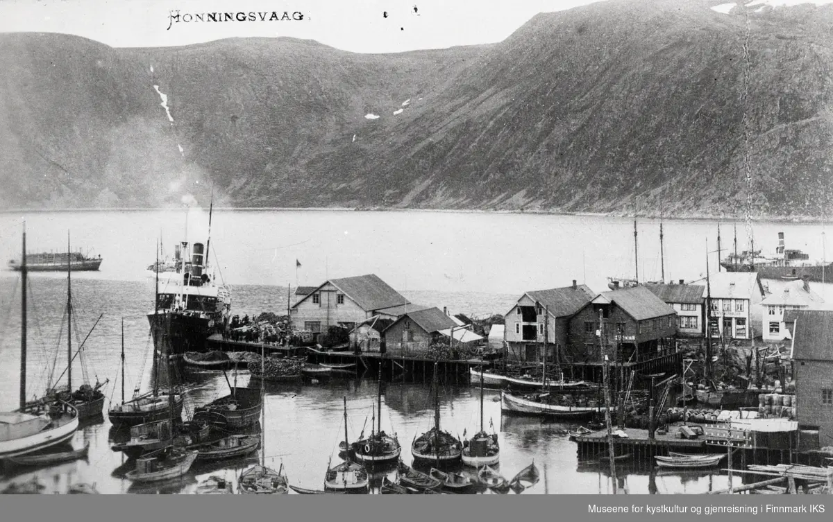 Postkort. Honningsvåg. Holmen med butikker. Hurtigruta ankommer dampskipskaia. Fiskebåter, Nordlandsbåter og fiskehjeller i forgrunnen. Ca. 1930-1935.