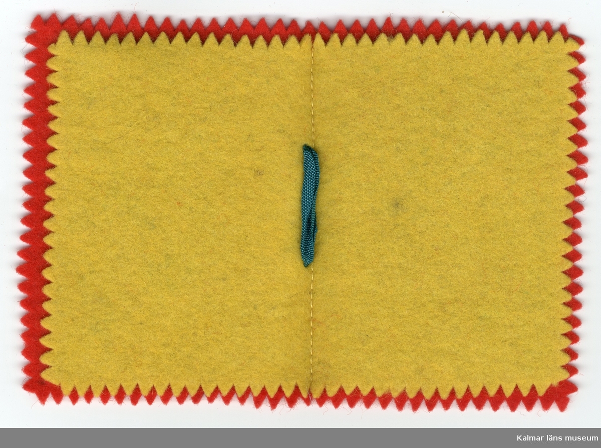 KLM 28082:178:1 Nålbok, av textil, ylle och konstmaterial. Pärm, ylle, röd, framsida, garnerad i blått, grönt och gult, i form av hjärta, blad och stjärnor, insida, blad, gult. Nålbok, pärm och innerblad sicksackklippta, ihopsydd på mitt och band, grönt, bildar rosett på bokrygg.