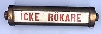 Cylinderformad skylt i mässing för personvagn med roterbar skylt av trä. Skylten är vit med röd text.
"ICKE RÖKARE"  "RÖKARE"  "ABONNERAD"  "DAMER"