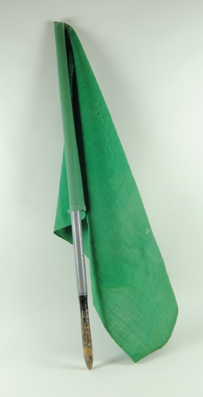 Signalflagga med flagga av grönt tyg och gråmålat svarvat skaft med svart handtag.
