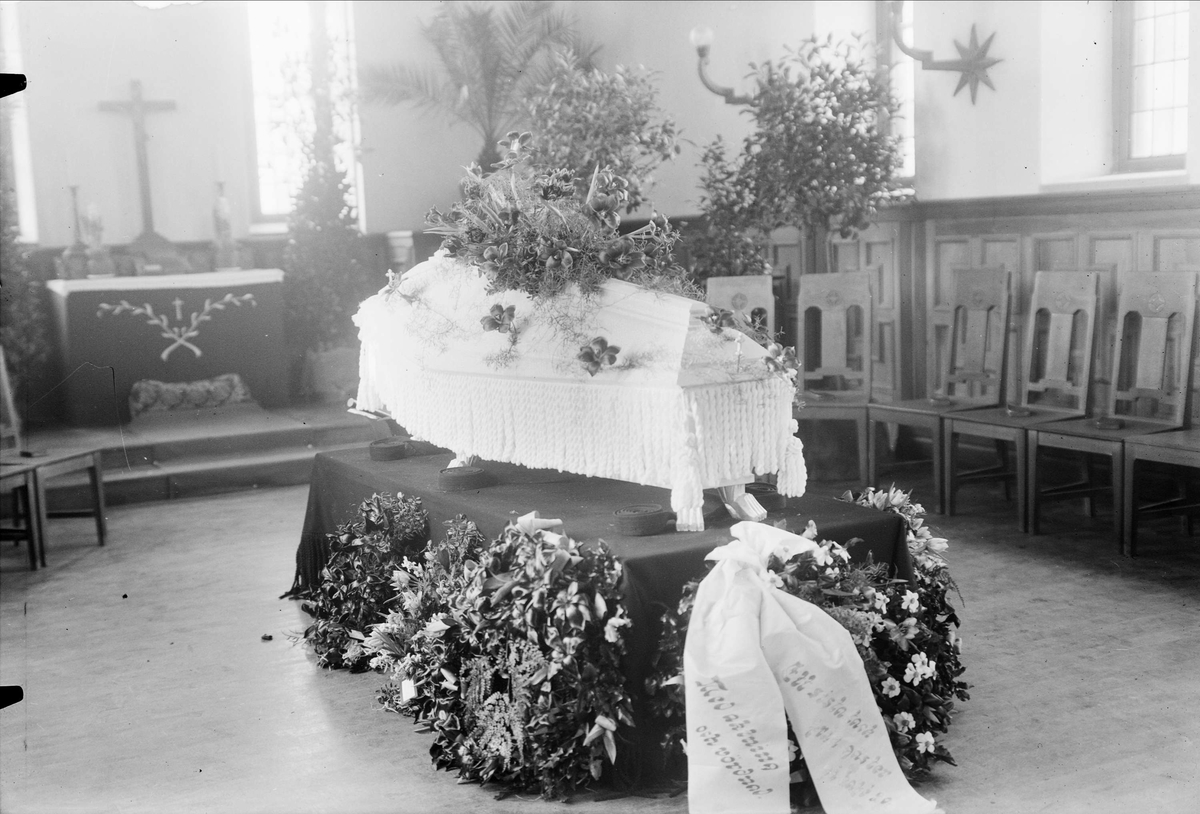 Begravning. Ljus kista med omgiven av blommor och kransar.