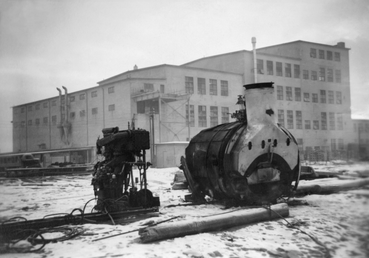 Dampmaskinen fra slepebåten «Axel», som tilhørte Skiensvassdragets Fellesfløtningsforening.  Båten ble satt i drift i 1903, og gikk i hovedsak som tømmersleper på Vestvatna.  Fartøyet ble ombygd fra damp- til dieseldrift vinteren 1953-54.  Ombyggingsarbeidet skjedde ved Knardalstrand Slip & Verft i Porsgrunn, som hadde mange oppdrag for Skiensvassdragets Fellesfløtningsforening.  Fotografiet er tatt på Porsgrunn havnevesens kai, som lå på motsatt side av elva i forhold til det nevnte verftet.  Industribygget i bakgrunnen er fabrikklokalene hvor A/S Sanitærporselen (opprinnelig et datterselskap av Porsgrund Porselænsfabrik) i 1950 startet produksjon av vannklosetter og vaskeservanter med mer. 