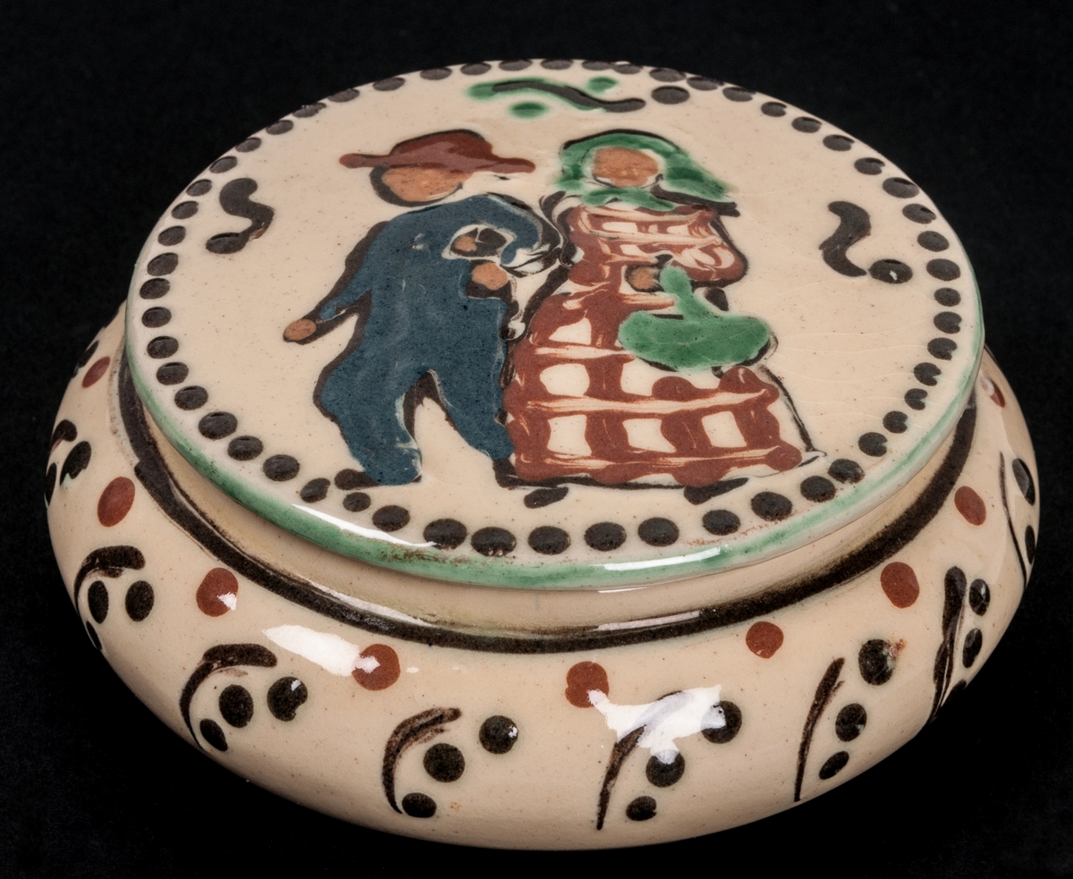 Bonboniere, keramik, Kählerkeramik. Gul glasyr. Dekor i brunt, blått och grånt. På locket två figurer, en man och en kvinna.