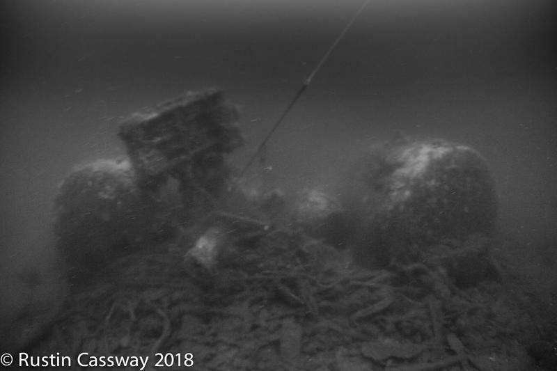 Uklart svart-hvitt bilde av dampkjeler på skipsvrak under vann.