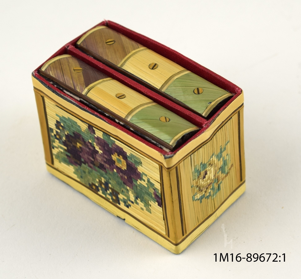 Två små kortlekar som förvaras i låda i formen av en liten bokhylla med ett fack för vardera kortlek. Blommotiv på lådans alla sidor.