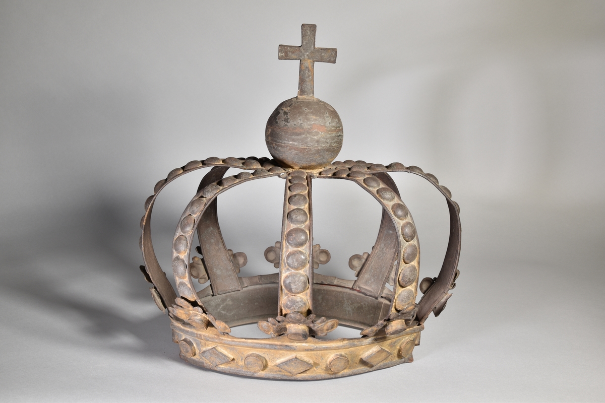 Skylt, oval, i form av tredimensionell krona med 8 bågar och krönt med klot och kors. Rester av färg.