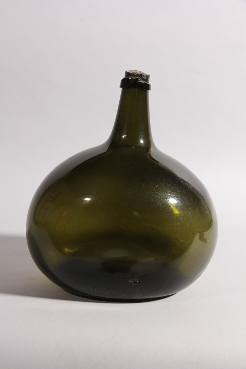 Flaska av grönt glas, rund med tillplattade sidor och hög hals.