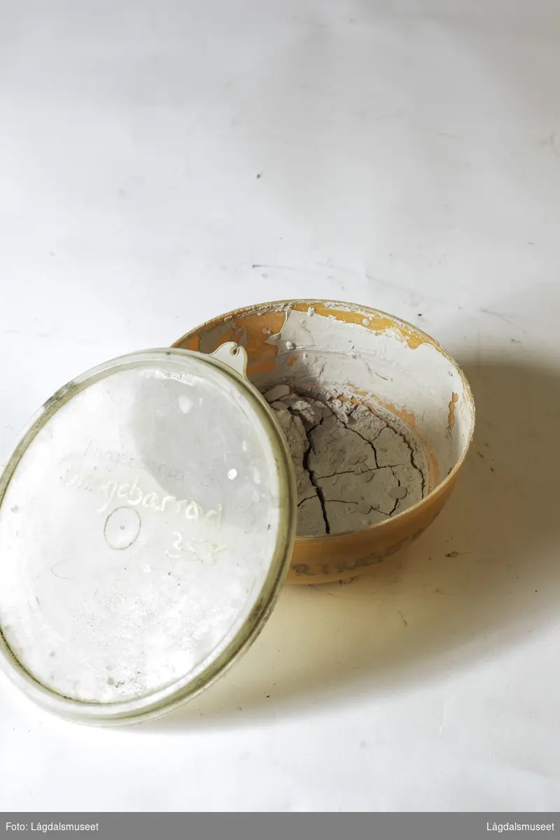 Plastbolle med lokk med uttørket pipeleire i fargen bringebærrødt. Pipeleiren ble brukt til begitting av keramikken.