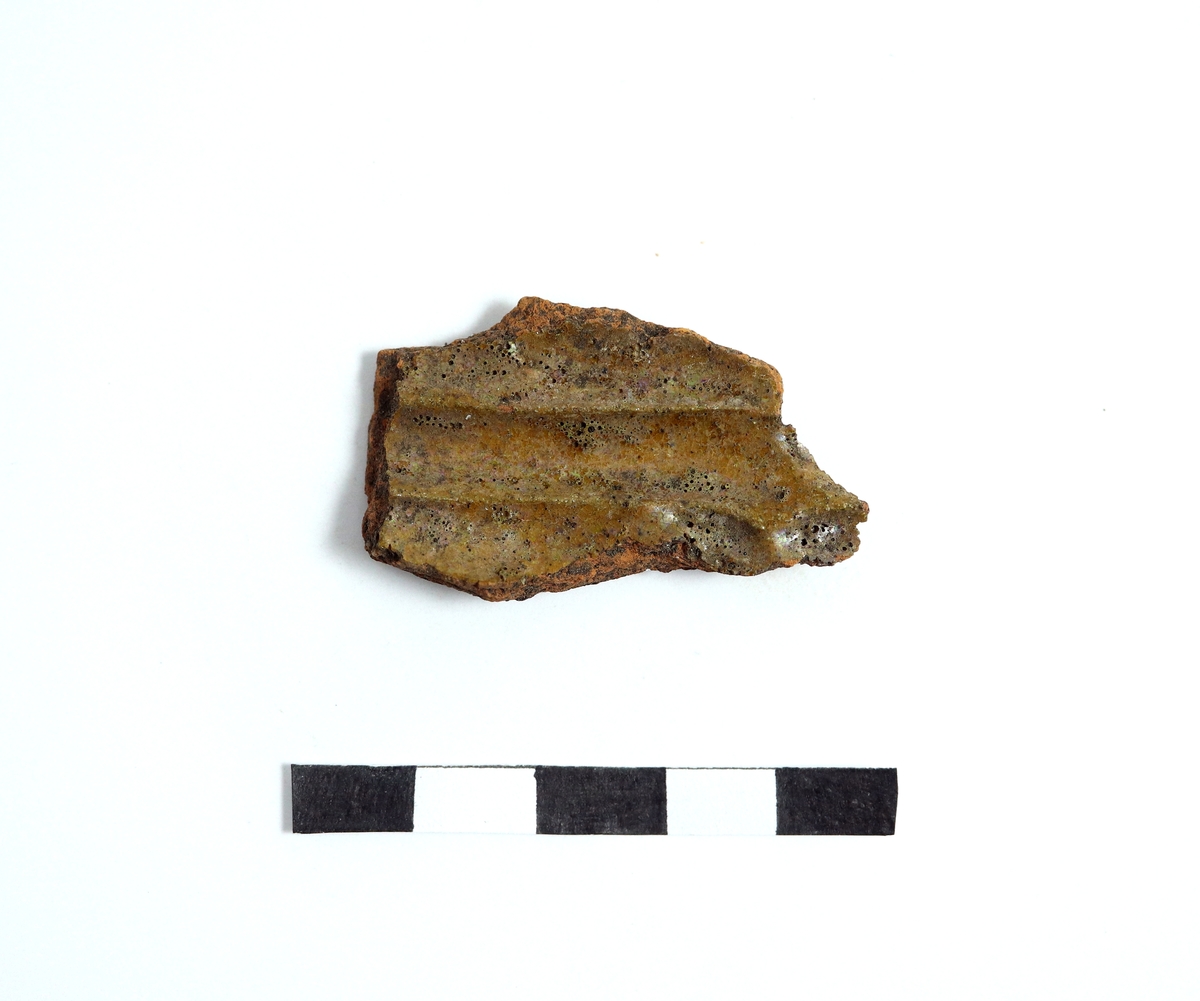 Fragment av en del till en aladobform av yngre rödgods. Insidan glaserad och formad med parallella fördjupningar. Utsidan spjälkad. Se även M 17000-2567. Troligen tillverkad under tidigt 1600-tal.