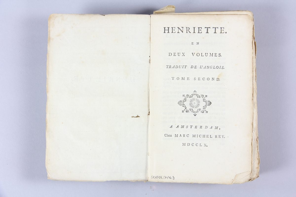 Bok, pappband, "Henriette", del 2, tryckt 1760 i Amsterdam. Pärmar av  gråblått papper, rygg med etikett med bokens titel, delvis svårtolkad, samt samlingsnummer. Oskuret snitt.