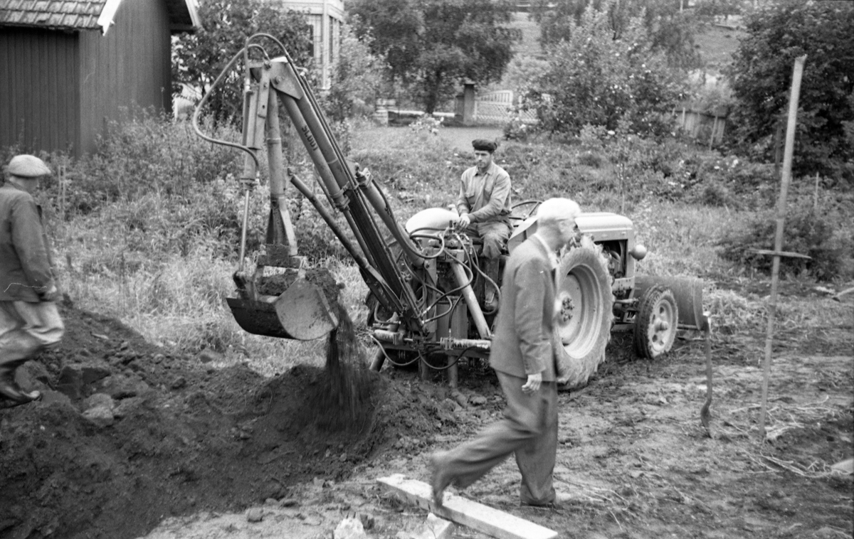 Grøftegraving med traktorgraver, trolig fra anleggsarbeide for Skreia Vannverk september 1953. To bilder der mannen i forgrunnen til høyre på det første bildet er Paul O. Aas. De andre mennene er ikke identifisert.