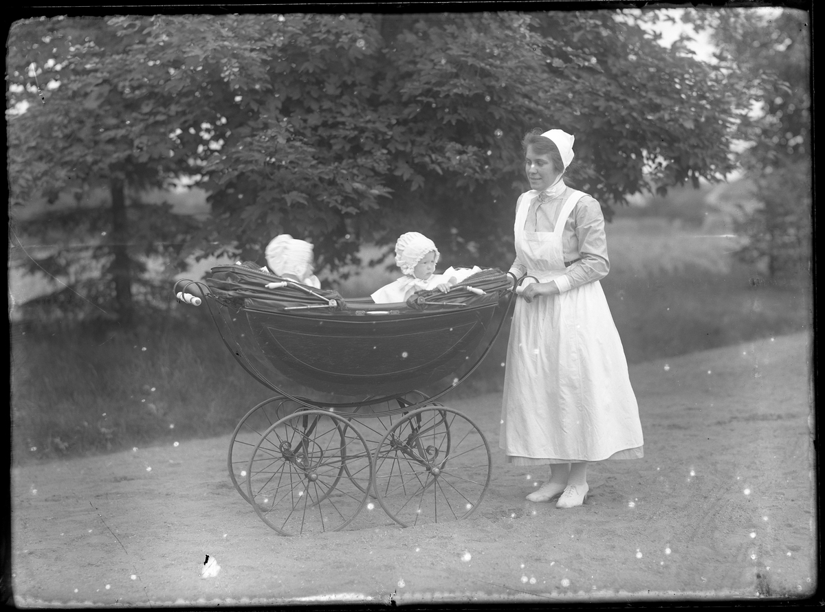 En sköterska kör en barnvagn med barnen Tollstadius på en gräsmatta. Troligen Ester och Birgit Tollstadius.