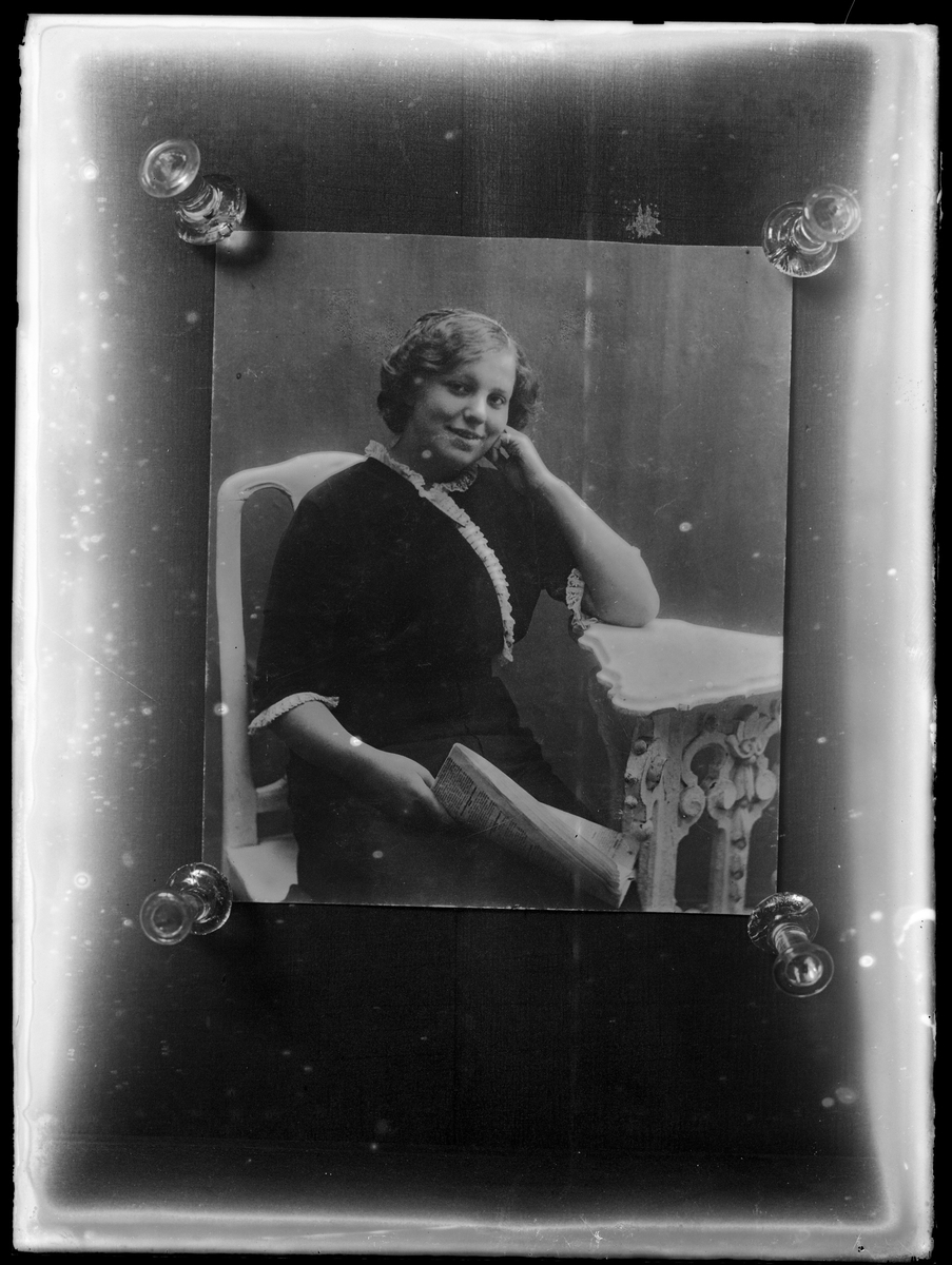 Reprofotografi av porträtt av okänd kvinna med tidning i handen sittandes vid ett bord.